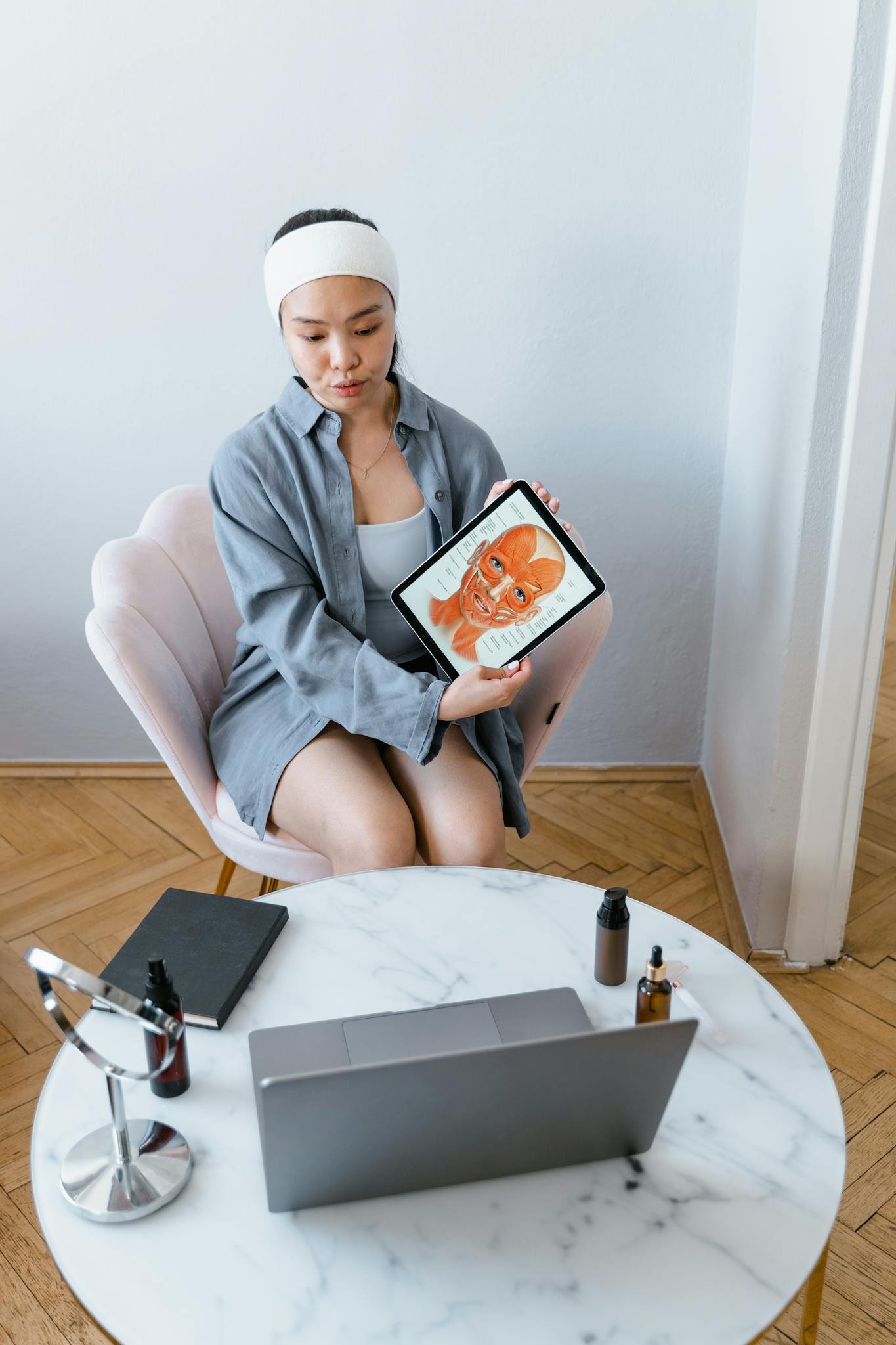 Woman demonstrating skincare procedure through a virtual consultation using a tablet.