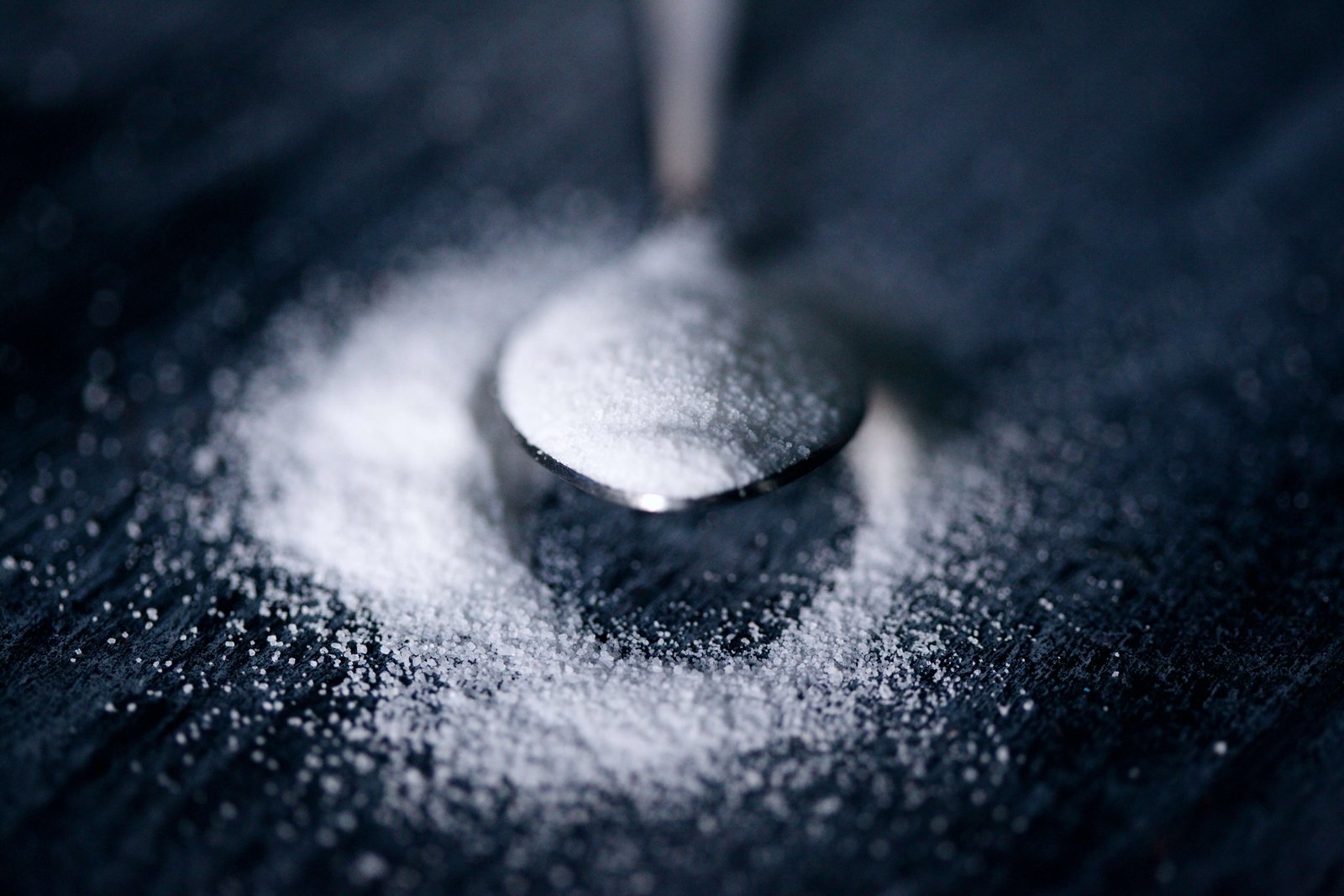 Refined sugar spoon close-up — dietary sugar spikes insulin and triggers acne-related hormonal pathways